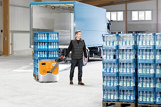 Man operating electric pallet jack moving pallets of bottled water inside warehouse near open delivery truck