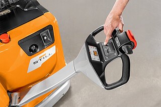 Hand operating the control handle of an orange STILL machine with buttons and a display